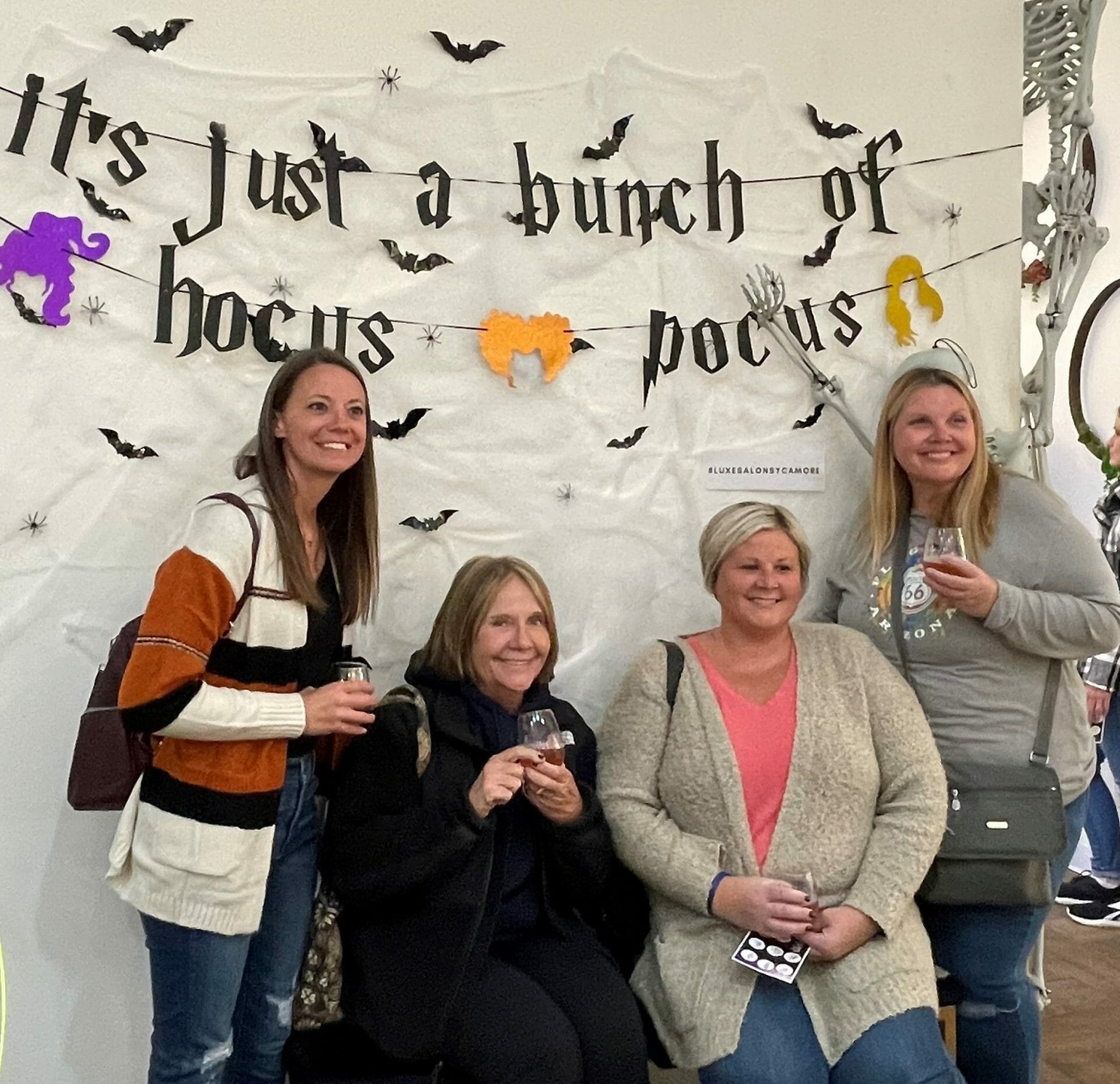 Four woman in front of a sign that says "It's just a bunch of hocus pocus"