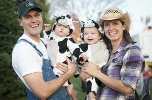 A smiling family with two parents and two babies dressed as cows.
