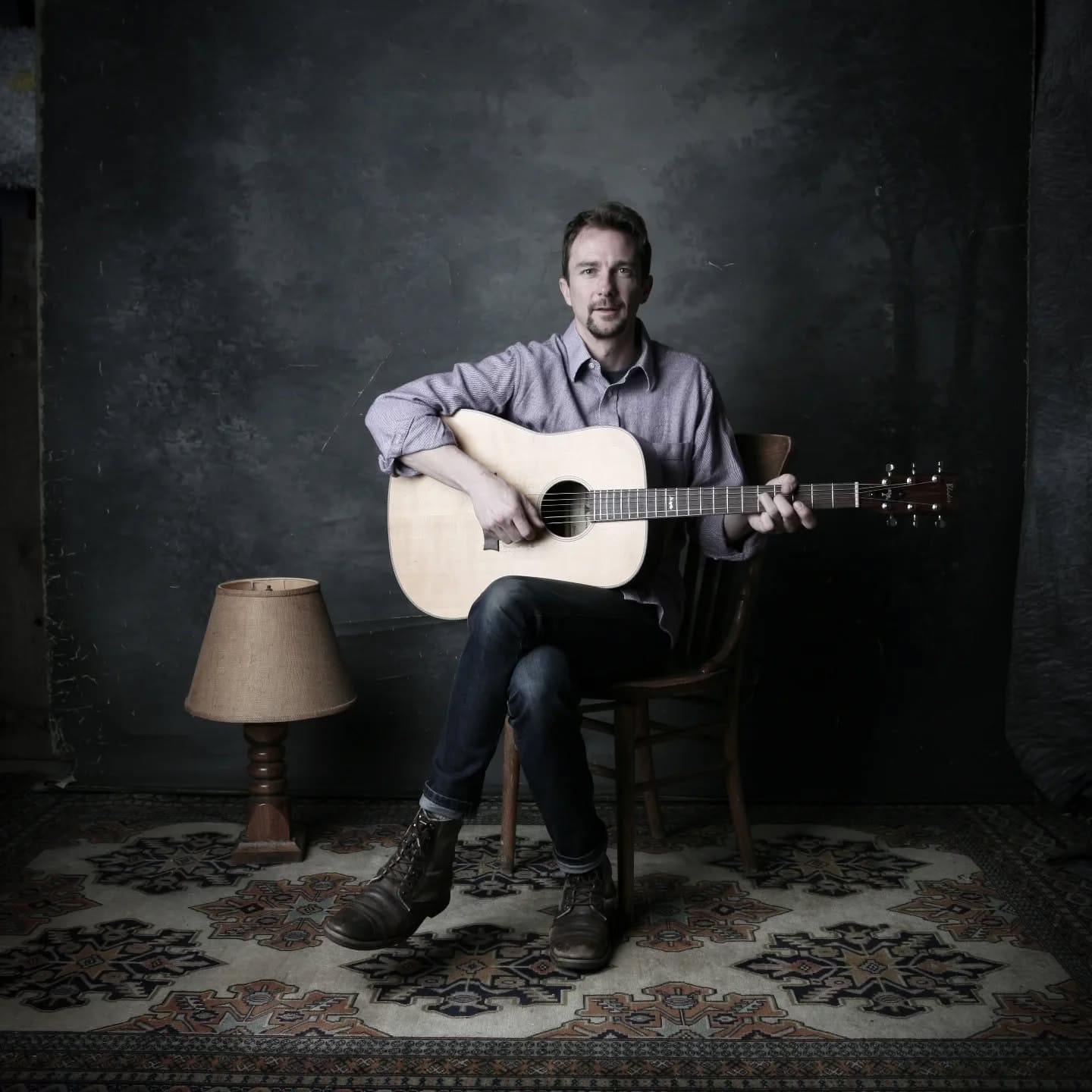 Pete Jive sitting on a stool and holding a guitar